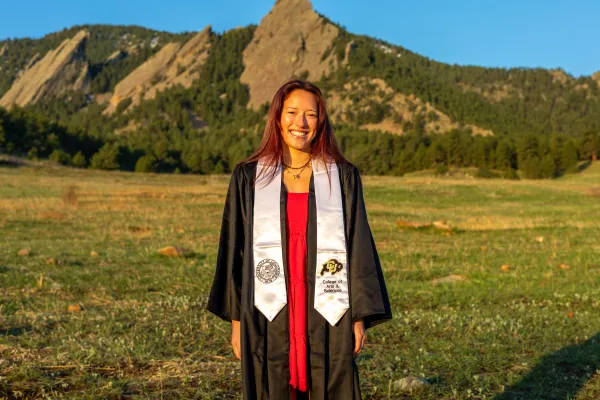 Arapahoe County worker in graduation gown in front of mountain 