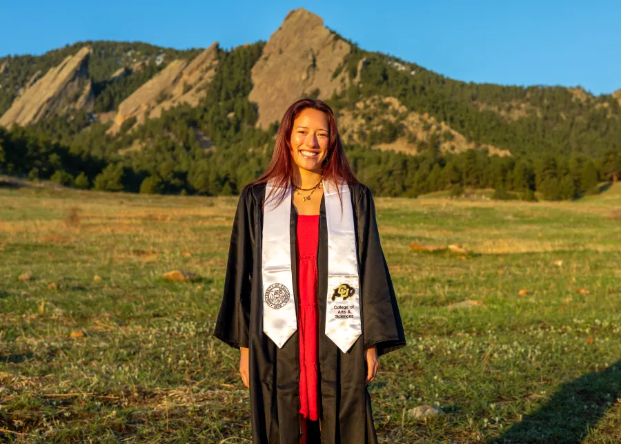 Arapahoe County worker in graduation gown in front of mountain